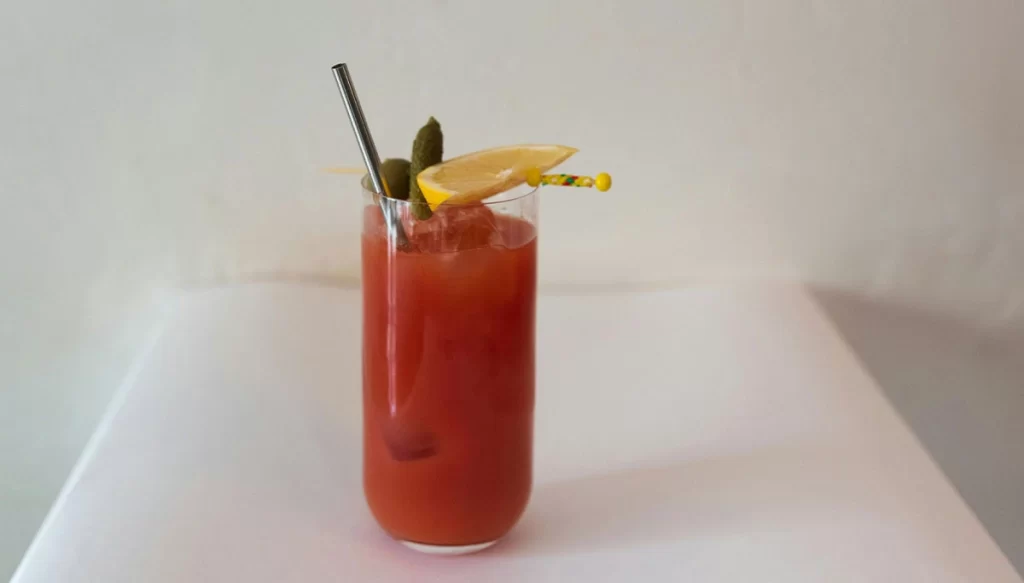a glass of tomato juice with a fruit garnish on a white table