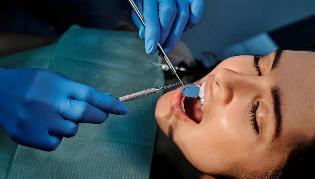 dental patient in chair while dentist uses dental tools to examin her mouth