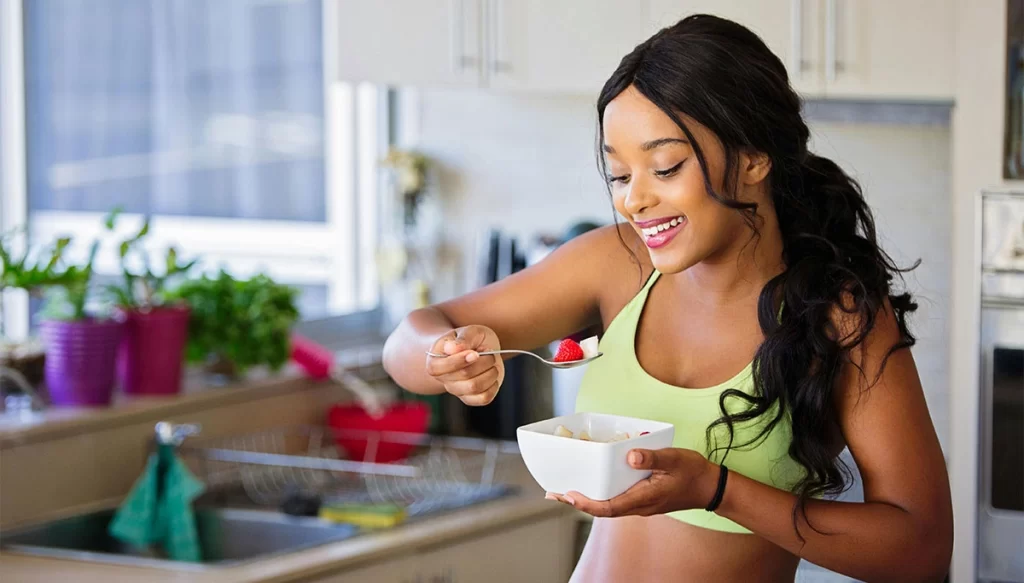 young woman in her kitchen eating a raspberry with a smile on her face.