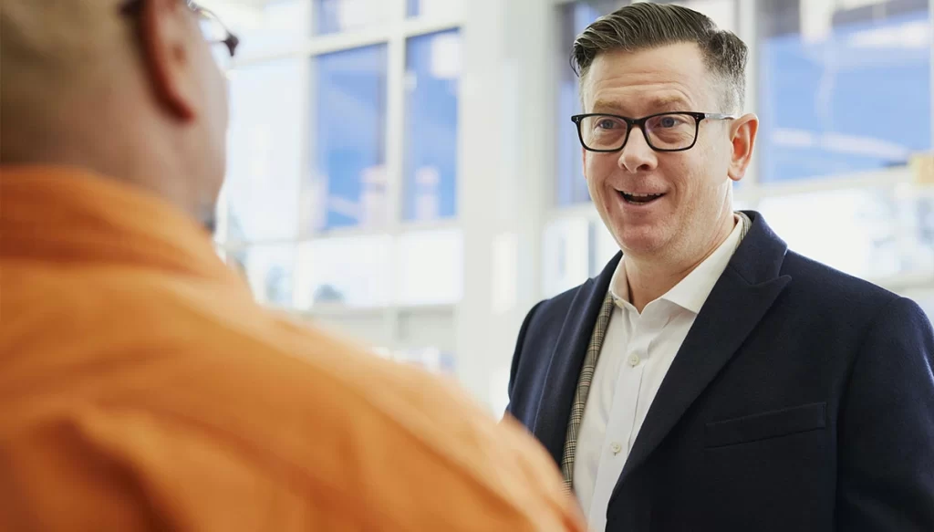 A man dressed business casual having a conversation with another man in an office setting.