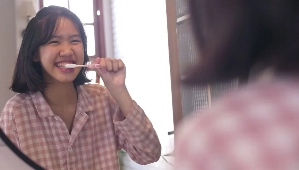 young woman brushing her teeth infront of a mirror