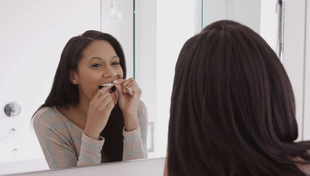 woman flossing her teeth in the mirror