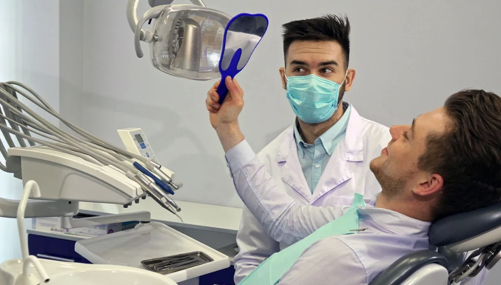 male dental patient looks at his face in a handhel mirror while dentist watches